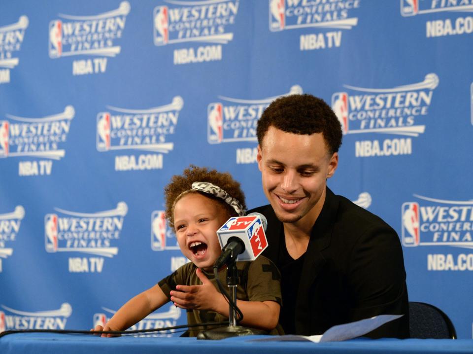 Stephen Curry's daughter laughs while sitting on his lap during a press conference in 2015.