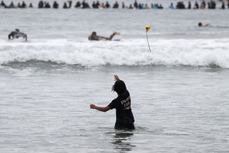 A boy throws a rose into the oceanat The Black Girls Surf paddle-out in memory of George Floyd, who died in Minneapolis police custody, in Santa Monica