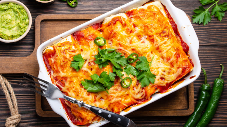 Enchiladas in white baking dish on wooden cutting board