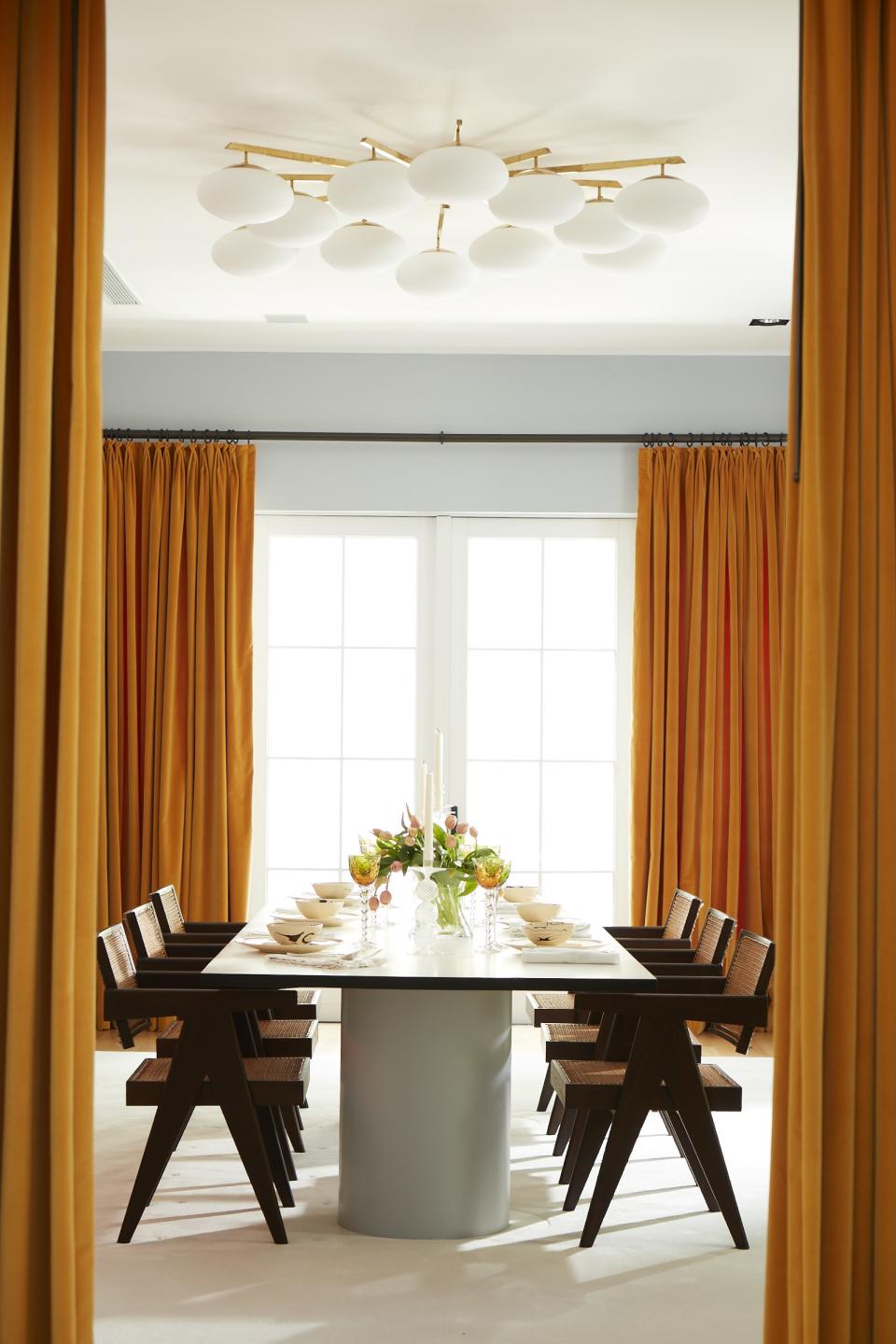 A brass-and-glass chandelier hangs over the dining room, where 1950s Pierre Jeanneret chairs stand at a table by Ana Kraš for Matter Made. The curtains are of a Zak + Fox velvet.