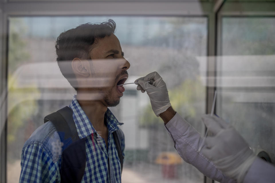 A health worker takes a swab sample to test for COVID-19 at a government hospital in Noida, a suburb of New Delhi, India, Wednesday, April 7, 2021. India hits another new peak with 115,736 coronavirus cases reported in the past 24 hours with New Delhi, Mumbai and dozens of other cities imposing night curfews to check the soaring infections. (AP Photo/Altaf Qadri)