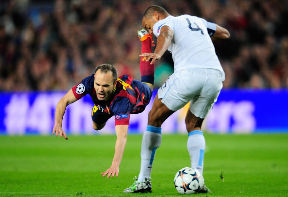 Barcelona's Andres Iniesta, left, falls in front of Manchester City's Vincent Kompany during a Champions League, round of 16, second leg, soccer match between FC Barcelona and Manchester City at the Camp Nou Stadium in Barcelona, Spain, Wednesday March 12, 2014. (AP Photo/Manu Fernandez)