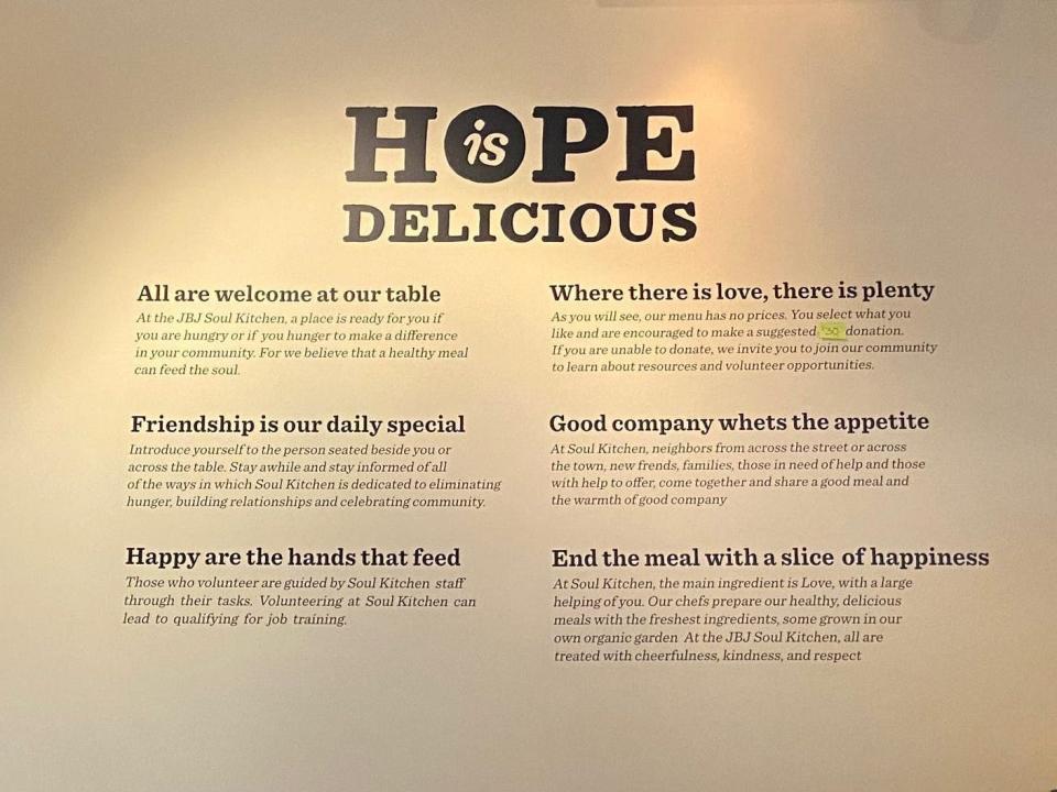 A beige wall with black word decals reading "hope is delicious," "all are welcome at out table," "friendship is our daily special," "happy are the hands that feed," "where there is love, there is plenty," "good company whets the appetite," and "end the meal with a slice of happiness."