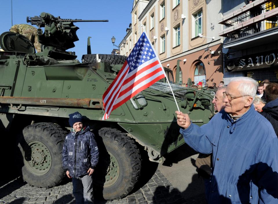 In this Tuesday, March 24, 2015, photo, a man holding a U.S. flag walks past a U.S. Army Stryker armored vehicle from the 3rd Squadron of the 2nd Cavalry Regiment, during their stop to meet local residents on the Kosciuszko Market Square in Bialystok, Poland.