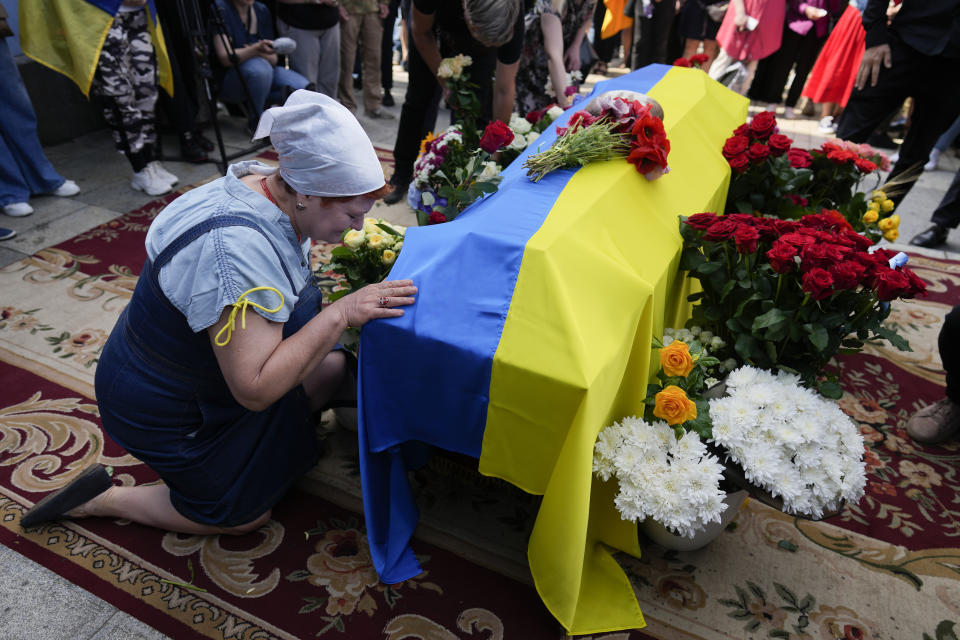 CAPTION CORRECTS FAMILY NAME OF SOLDIER A woman kneels at activist and soldier Roman Ratushnyi's coffin during his memorial service in Kyiv, Ukraine, Saturday, June 18, 2022. Ratushnyi died in a battle near Izyum, where Russian and Ukrainian troops are fighting for control of the area. (AP Photo/Natacha Pisarenko)