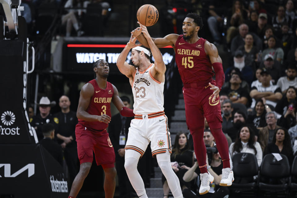 Cleveland Cavaliers' Donovan Mitchell (45) steals the ball from San Antonio Spurs' Zach Collins (23) as Cavaliers guard Caris LeVert (3) watches during the first half of an NBA basketball game, Saturday, Feb. 3, 2024, in San Antonio. (AP Photo/Darren Abate)