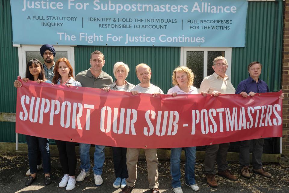 A group of postal workers hold a long red sign that reads 'Support Our Sub-Postmasters'.