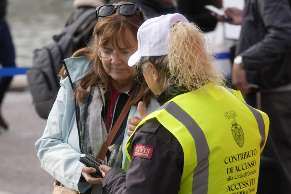 Una asistente comprueba el código de acceso de una turista ante la principal estación de tren de Venecia, el jueves 25 de abril de 2024. Ante la mirada de los medios del mundo, la frágil ciudad ribereña de Venecia inició un programa piloto el jueves para cobrar una cuota de entrada de unos 5 euros (unos 5,35 dólares) a los que visiten el lugar sólo por un día. (AP Foto/Luca Bruno)