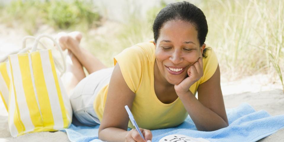 black woman doing crossword puzzle on beach