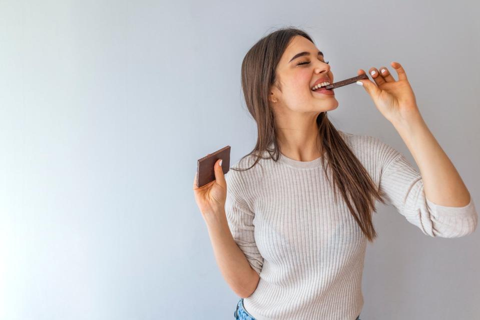 Person takes a bite of a candy bar while standing in front of a white wall.