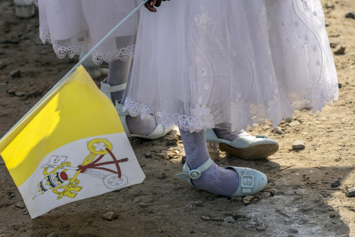 A young girl holds a Vatican flag and rocks on her shoes after standing for a long time prior to the arrival of Pope Francis at the St. Theresa Cathedral in Juba, South Sudan, Saturday, Feb. 4, 2023. Pope Francis is in South Sudan on the second leg of a six-day trip that started in Congo, hoping to bring comfort and encouragement to two countries that have been riven by poverty, conflicts and what he calls a "colonialist mentality" that has exploited Africa for centuries. (AP Photo/Ben Curtis)