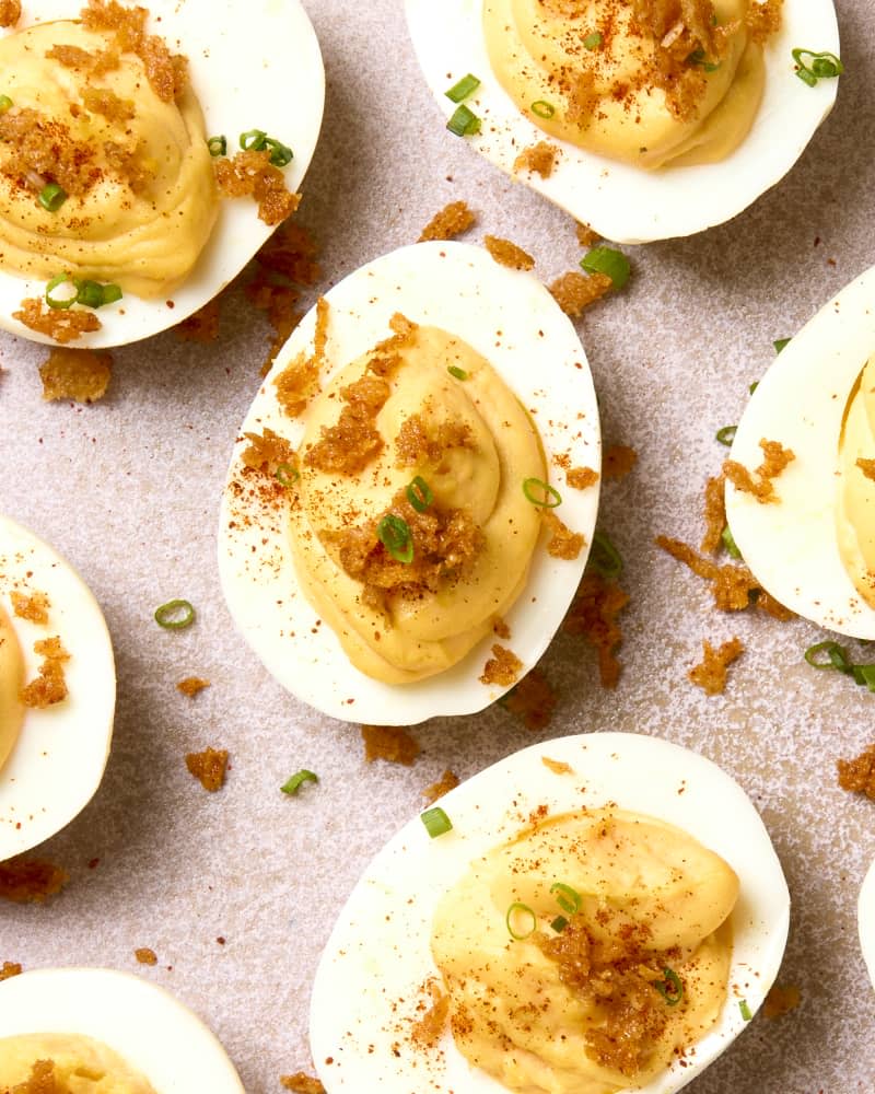 overhead shot of deviled eggs on a light pink plate, topped with toasted panko, green onion and paprika.