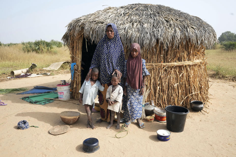 Aisha Ali, 40, stands with her children outside the hut where she found refuge from the floods in Darayami, northeastern Nigeria, Wednesday Oct. 26, 2022. When floodwaters reached her hut made of woven straw mats and raffia palms, she packed up what belongings she could and set off on foot with her eight youngest children. "While the flood was trying to destroy things, we were trying to save ourselves," she said. Four of her children perished. (AP Photo/Sunday Alamba)