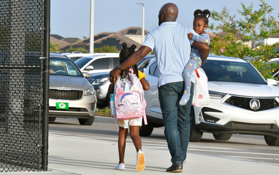 Ryan Fuller walks his 7-year-old daughter Reagan to her 2nd grade class, while carrying daughter Noelle, 4.  Back to school. Parents and students arriving at Viera Elementary School early Wednesday morning. August 10 was the first day for the new public school year in Brevard County.