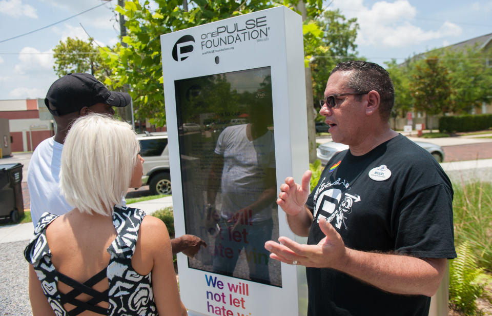 Miguel, a volunteer from Disney, explains how the new digital guestbook kiosk works to visitors at the Pulse memorial in Orlando, Florida on June 4, 2018.