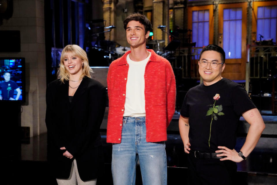 Chloe Fineman in a black outfit, Michael Longfellow in a red jacket and jeans, and Bowen Yang in a black shirt with a rose printed on it, standing together