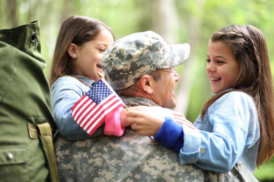 family welcomes home a usa army soldier  the children excitedly hug father holding american flags