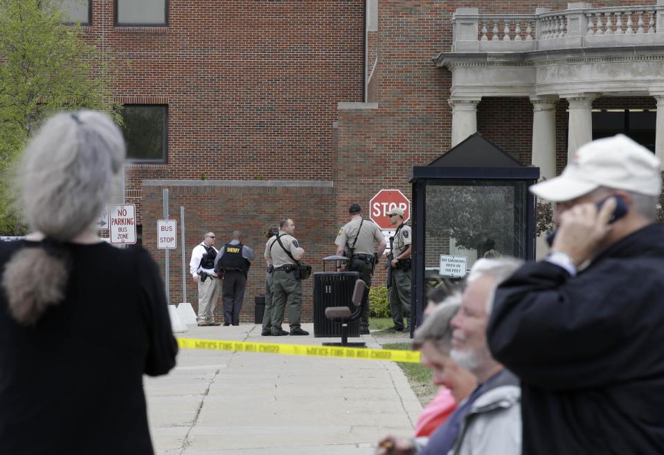 People watch police officials as they wait outside a Veterans Affairs hospital after they were evacuated, Monday, May 5, 2014, in Dayton, Ohio. A city official says a suspect is in police custody after a shooting at the Veterans Affairs hospital that left one person with a minor injury. (AP Photo/Al Behrman)