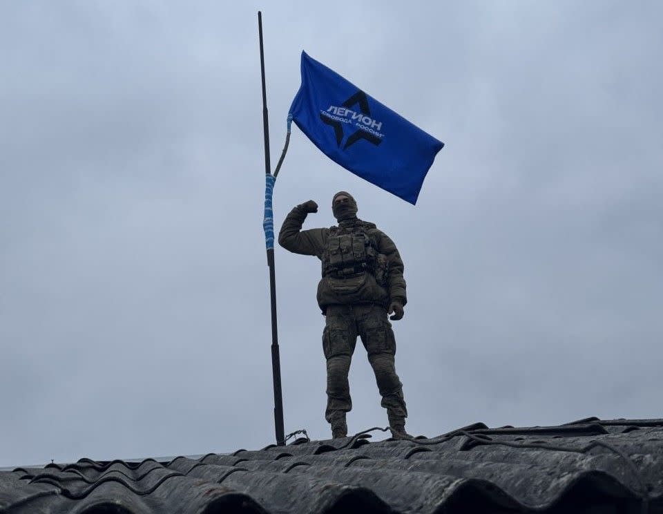 A Freedom of Russia Legion fighter holding next to his unit's flag. Photo published on March 17, 2024. Location unknown. (Freedom of Russia Legion/Telegram)