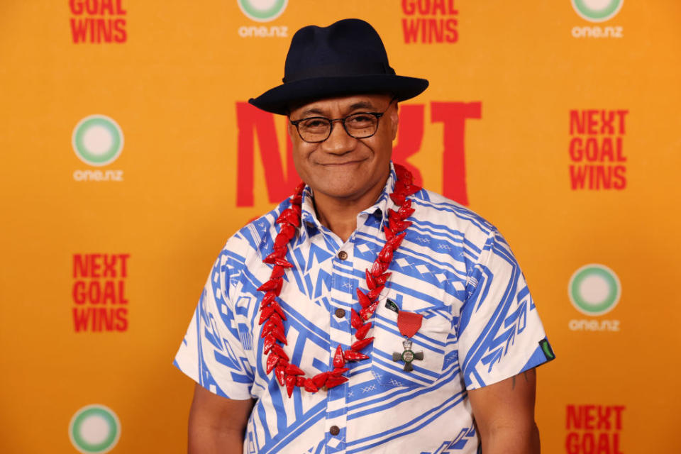 Person with hat and patterned shirt, flower lei necklace, posing in front of event backdrop