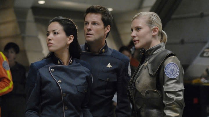 Three people standing inside a ship in a scene from Battlestar Galactica.