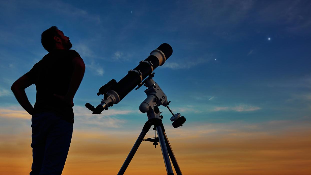  a person looking up at the night sky beside a telescope 