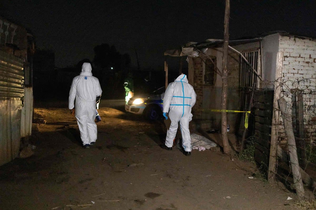 Members of the South African Police Service’s (SAPS) forensic department walk past a body covered with a blanket  (AFP via Getty Images)