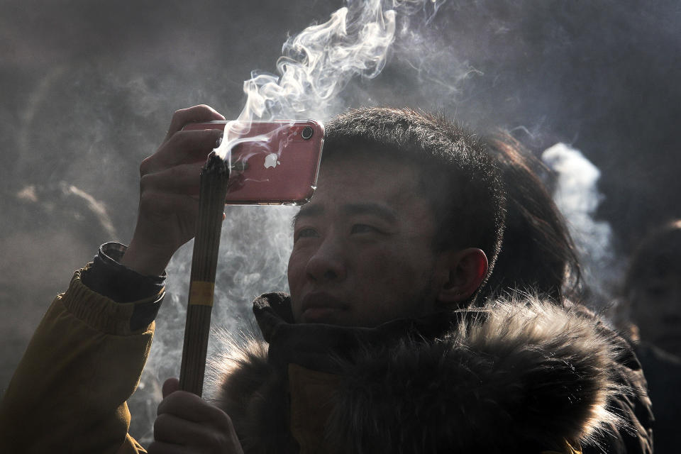 In this Tuesday, Jan. 1, 2019, photo, a Chinese man uses iPhone to take picture as he prays for health and fortune on the first day of the New Year at Yonghegong Lama Temple in Beijing. Apple acknowledged that demand for iPhones is sagging, a warning likely to roil financial markets. It confirmed investor fears that the company's most profitable product has lost some of its luster. CEO Tim Cook said that iPhone sales fell well below projections, especially in China, amid a trans-Pacific trade war and concern over global economic weakness. (AP Photo/Andy Wong)