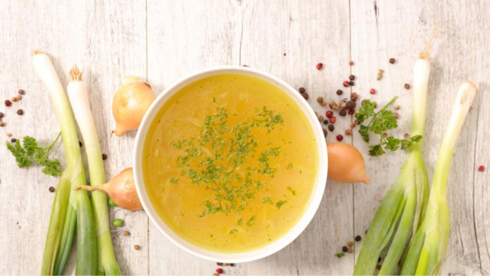 homemade chicken stock in white bowl with ingredients