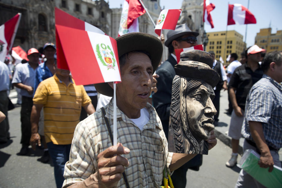 A man holding a Peruvian national flag and an Andean female face sculpture, attends a ceremony in front of government palace celebrating the World Court decision on the Peru-Chile maritime border, in Lima, Peru, Monday, Jan. 27, 2014. The United Nations' highest court set a maritime boundary between Chile and Peru on Monday, granting the latter a bigger piece of the Pacific Ocean but keeping rich coastal fishing grounds in Chilean hands. (AP Photo/Martin Mejia)