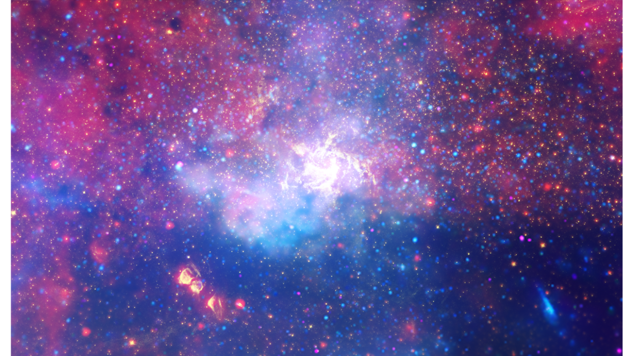  Annotated telescope image shows a tapestry of colors in shades of blue, purple, red, yellow, and white. Overlaid on the image are three sets of labels. In the upper right corner is the name of the object, Center of the Milky Way Galaxy, and the name of the telescopes used to capture the image: Chandra X-ray Observatory, Hubble Space Telescope, and Spitzer Space Telescope. At the center is a label that points to the smaller, amorphous region in white that reads, Sagittarius A-star. 