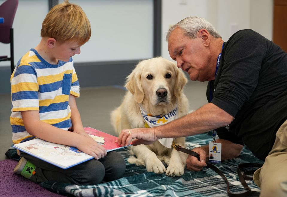 PJ Kelly, 8, reads to Paws and Think therapy dog Cooper and handler Sid Zachary on Wednesday, Nov. 8, 2023, after meeting IndyStar for an interview at Brownsburg Public Library. Paws and Think is a program where children can practice their reading in front of therapy dogs, which creates a more welcoming, less intimidating environment.