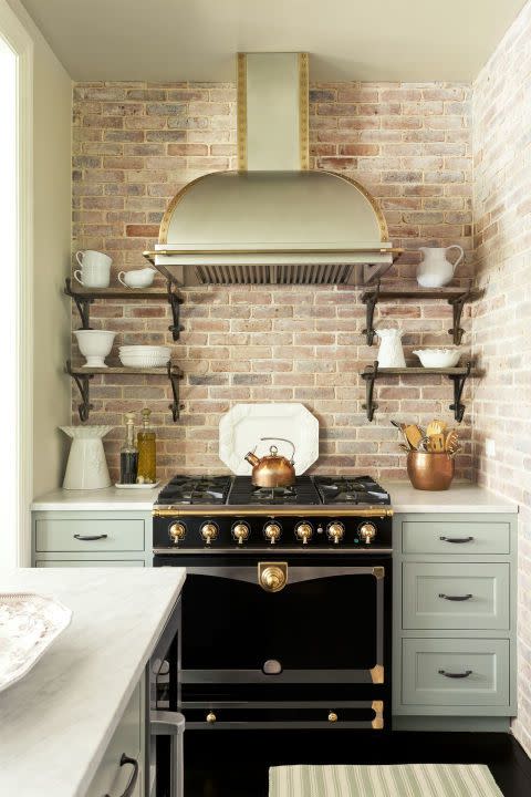 green kitchen cabinets with a black stove and brick backsplash