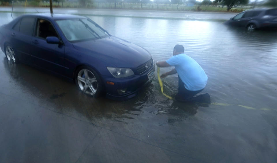 Mon Lun attaches a strap to his water stalled car before towing it out of receding flood waters in Dallas, Monday, Aug. 22, 2022. (AP Photo/LM Otero)