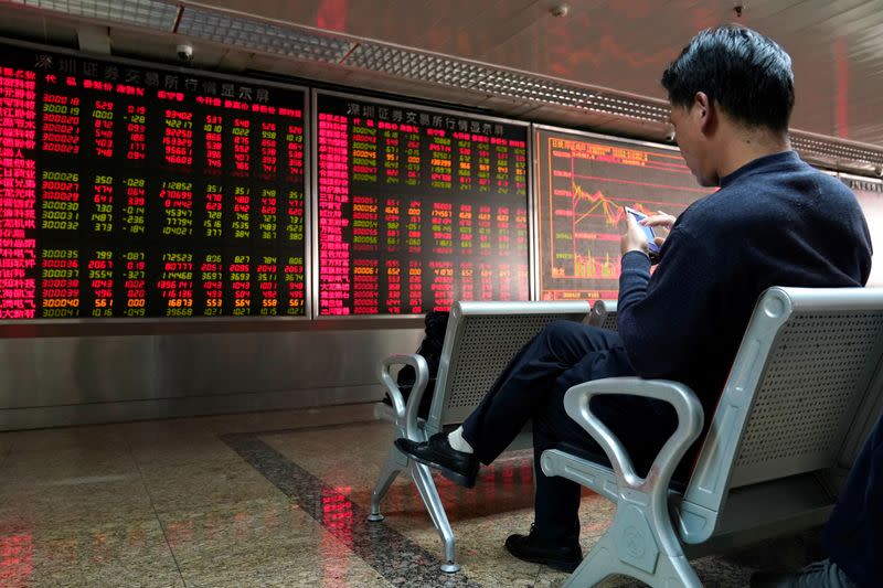 FILE PHOTO: An investor uses his mobile phone in front of a stock quotation board at a brokerage office in Beijing