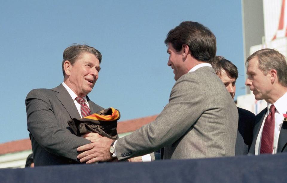 President Ronald Reagan shakes hands with baseball player Steve Garvey after receiving his gift of a San Diego Padres jacket during a trip to San Diego at a Reagan-Bush campaign rally in October 1984. California Sen. Pete Wilson stands at right.