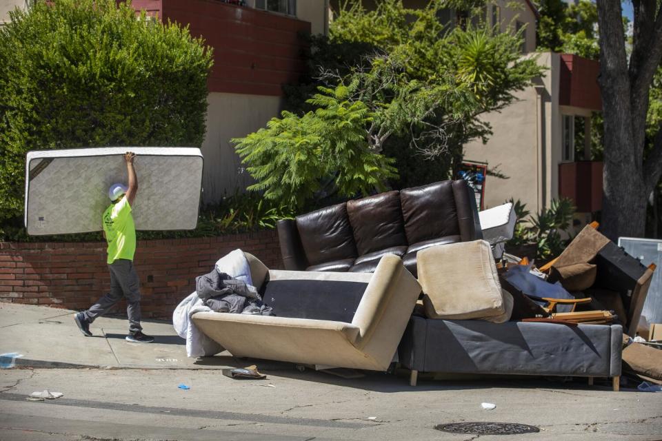 A man tosses a mattress on the sidewalk with a pile of other debris.