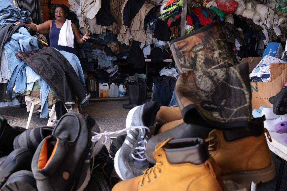 Nirvah Lamerique, 69, stands among the piles of jeans at her booth, which supplements her retirement income, on June 7, 2022. Her crowded booth has tables stacked with construction worker shirts and pants, work boots, army fatigues and rolls of industrial toilet paper.