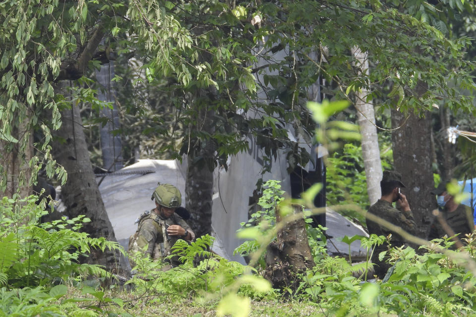 A soldier stands beside the tail of a Lockheed C-130 Hercules plane at its crash site in Patikul town, Sulu province, southern Philippines, Monday July 5, 2021. Philippine troops found the last five dead from the crash of the transport aircraft in the south, raising the death toll to 50 in the military's worst air disaster, officials said Monday. (AP Photo/Nickee Butlangan)