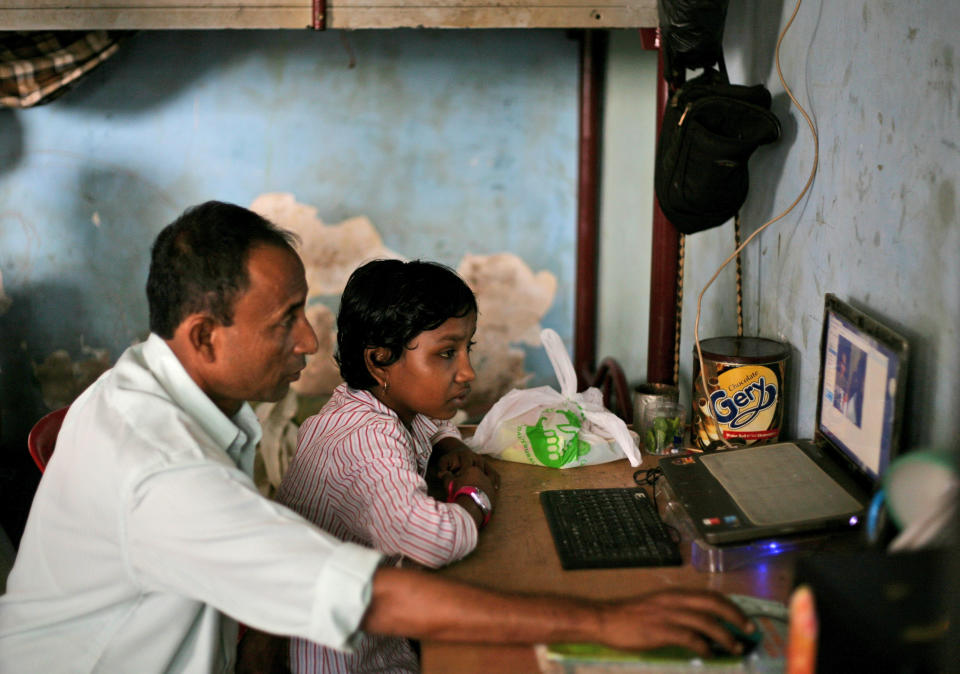 In this Oct. 20, 2013 photo, young ethnic Rohingya asylum seeker Senwara Begum, right, is helped by her foster father, Shamsul bin Sayed, to use Skype to talk to her family members in Myanmar from their temporary shelter in Medan, North Sumatra, Indonesia. "I'm fine," Senwara says, trying to sound upbeat. "I'm with a family that is taking good care of me. They love me. I'm learning things, English and religion." Her father reminds her to be a good girl. He is desperate to see his children again, but believes they are better off far away. (AP Photo/Binsar Bakkara)