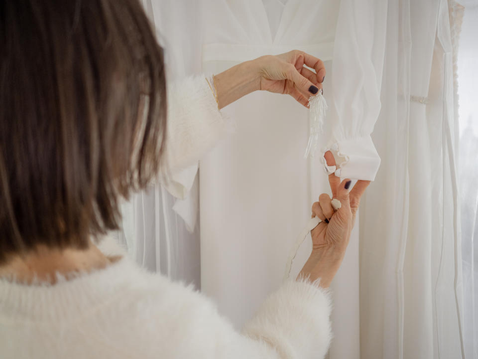 A person adjusts a white wedding dress sleeve in a bridal fitting room