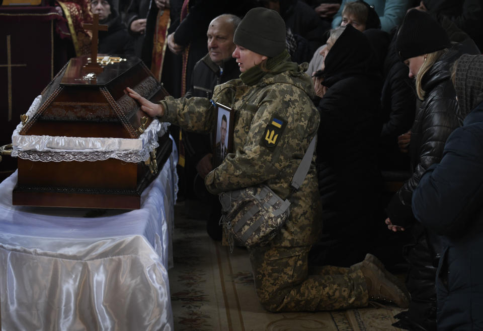 A person kneeling and wearing a military uniform touches the casket of a fallen soldier. 