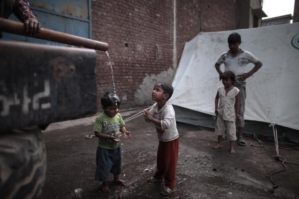 In this Thursday, March 14, 2013 photo, Pakistani Children wash themselves a water truck, next to their tent where they took shelter with their families, after their homes were destroyed by an angry Muslim mob in a Christian neighborhood in Lahore, Pakistan. Pakistan’s blasphemy law has become a potent weapon in the arsenal of Muslim extremists, who use it against adherents of minority religions. (AP Photo/Nathalie Bardou)