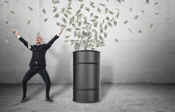 A barrel standing on a grey floor with money bursting out of it with a happy businessman celebrating next to it.