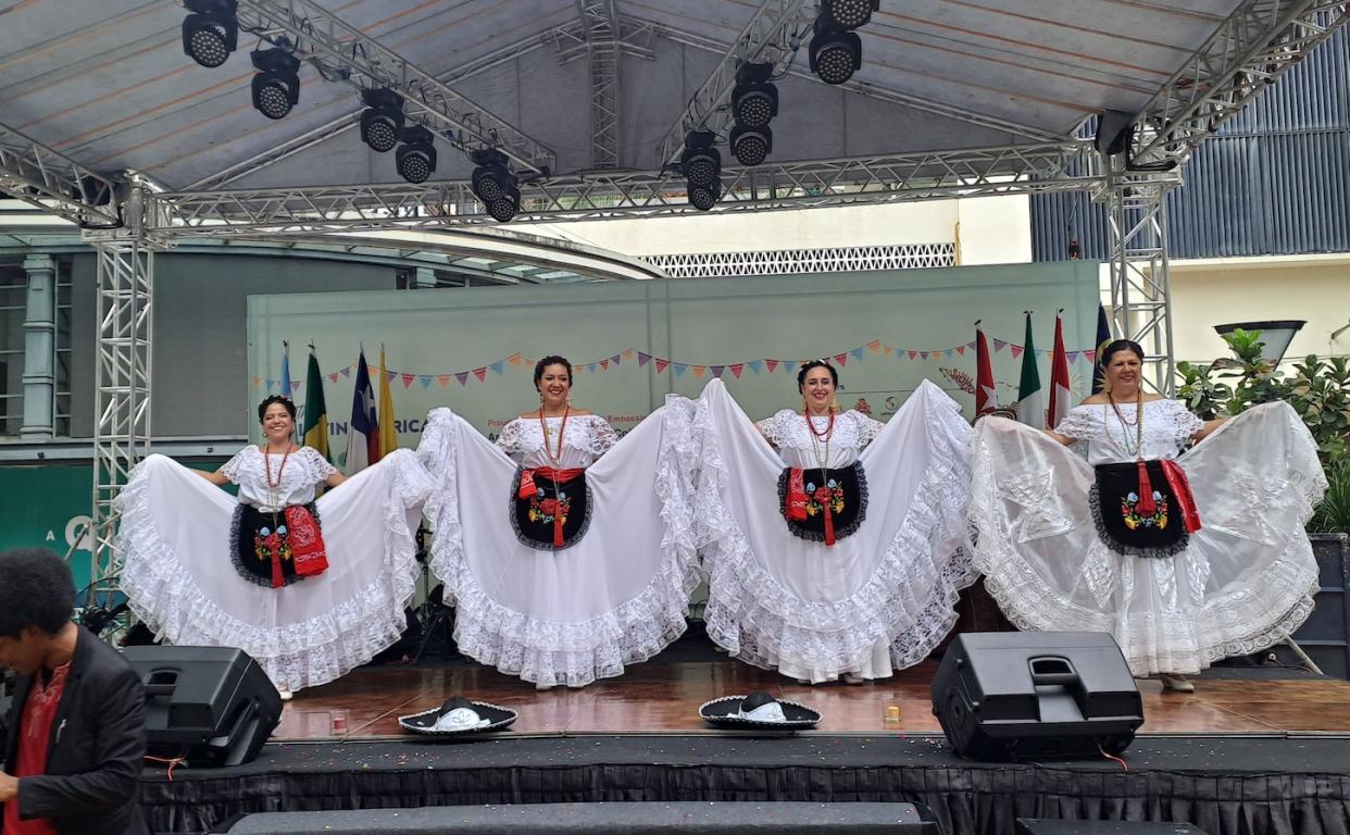 Four ladies dressed in white on a stage performing for the Latin America Dance Festical.