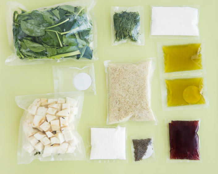 flat lay of meal kit ingredients in plastic bags on green background, spinach, rice, oil