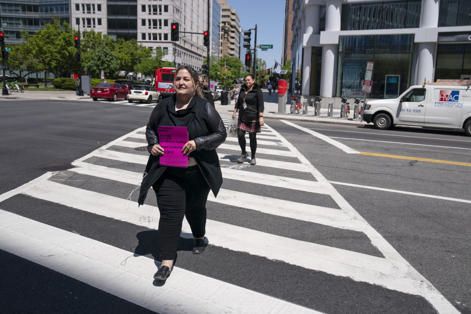 Melissa Byrne walks across Pennsylvania Avenue as she puts up posters near the White House promoting student loan debt forgiveness, Friday, April 29, 2022, in Washington. (AP Photo/Evan Vucci)