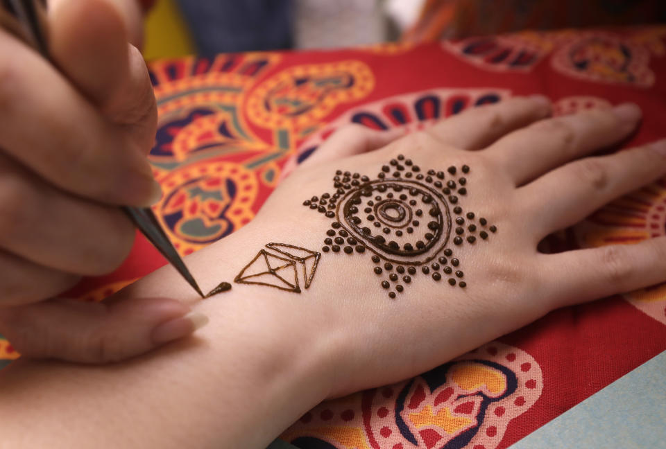 An artist applies henna on the hand or a woman during the Hindu festival of lights, Diwali, in Taipei, Taiwan, Thursday, Nov. 4, 2021. Millions of people across Asia are celebrating the Hindu festival of Diwali, which symbolizes new beginnings and the triumph of good over evil and light over darkness. (AP Photo/Chiang Ying-ying)