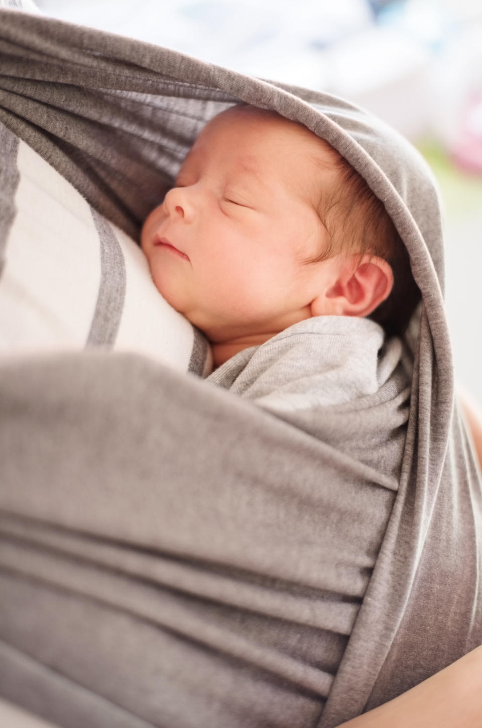 A newborn baby is peacefully sleeping while being cradled in a soft, gray wrap, close to the person holding them