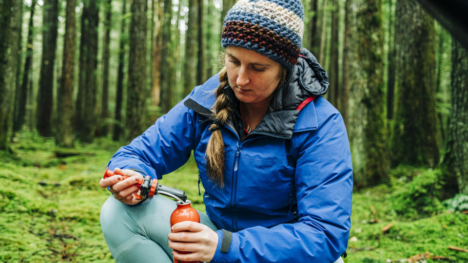 women instals the primer into a camp stove fuel canister while camping in a remote, coastal rainforest